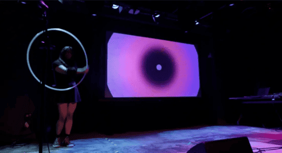 Performer with a hoop on stage beside a projected, real-time visual